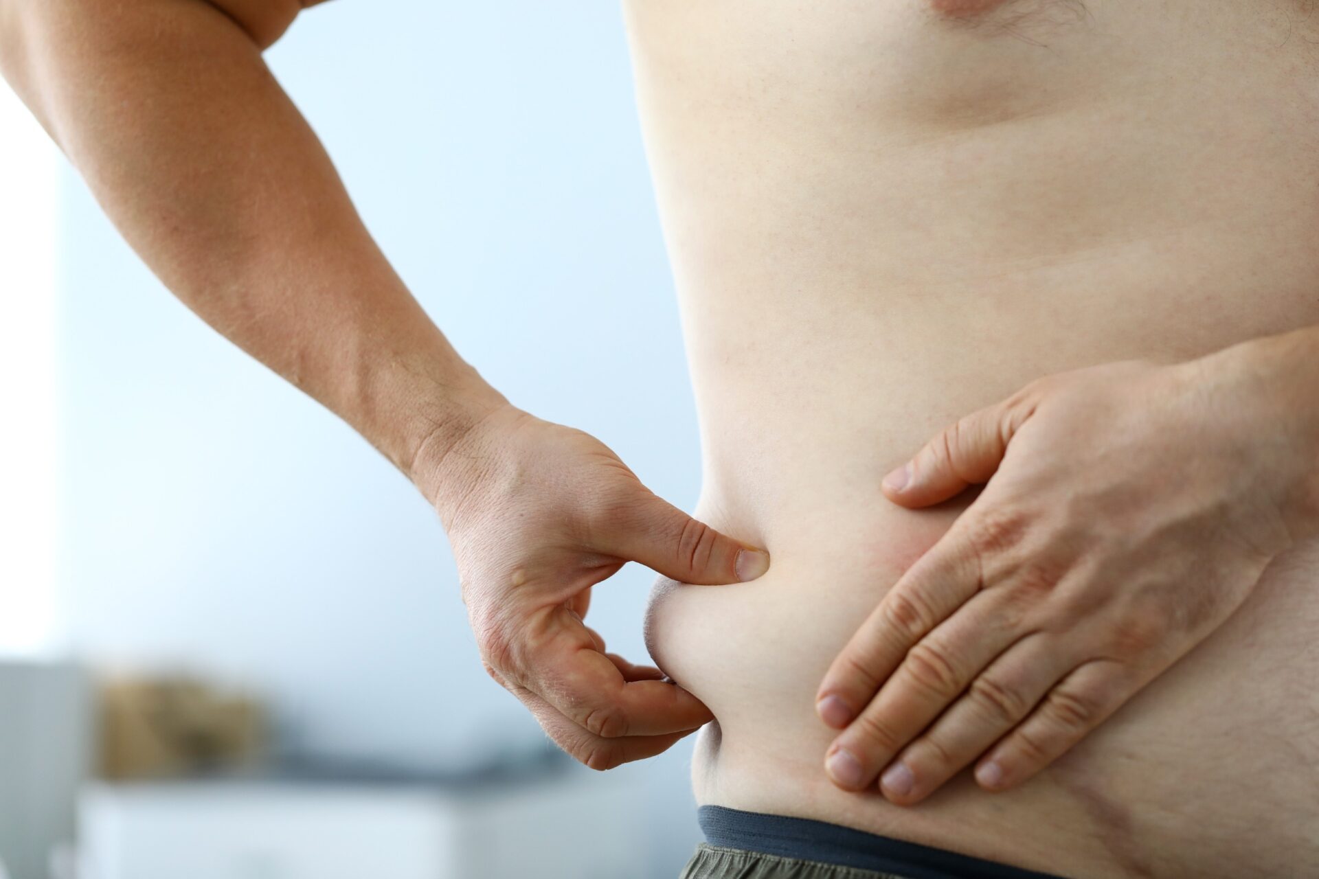 Close-up of male hand measuring thick waist to track down rate of getting plump and looking at overweight belly. Fat man preparing for training. Severe obesity and losing weight concept<br />
